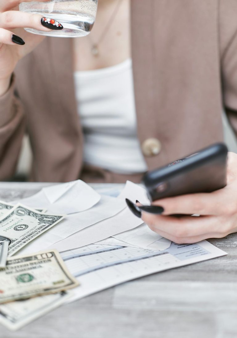 Close-up of a woman using a smartphone, holding cash, and managing finances indoors.